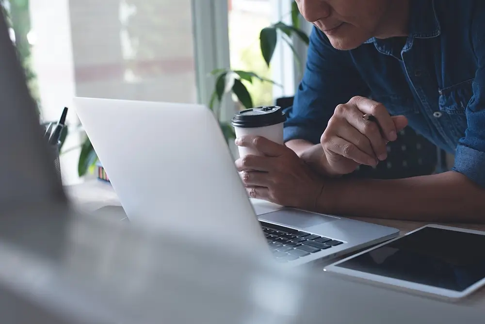 man reading off a computer with a coffee in his hand